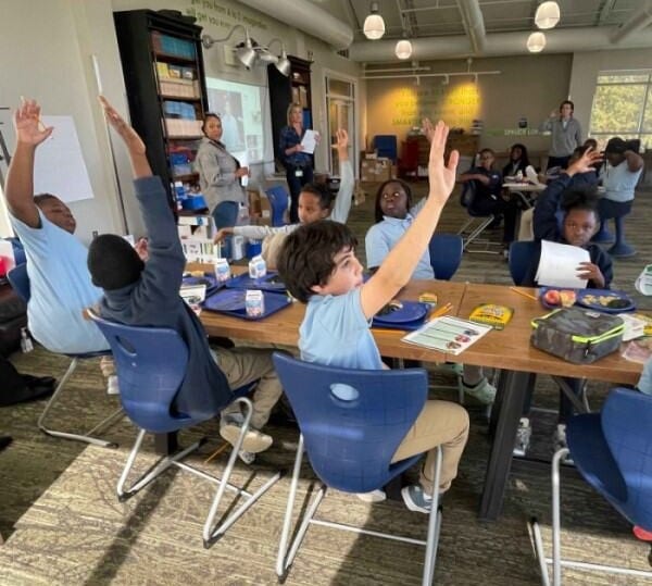 Students sitting around classroom table raising their hands