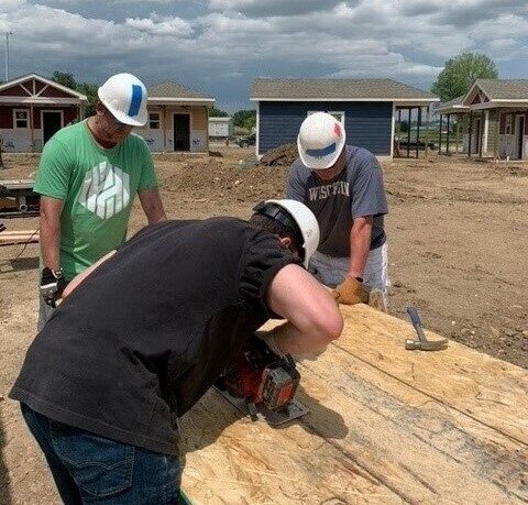 Three people wearing hats and building homes