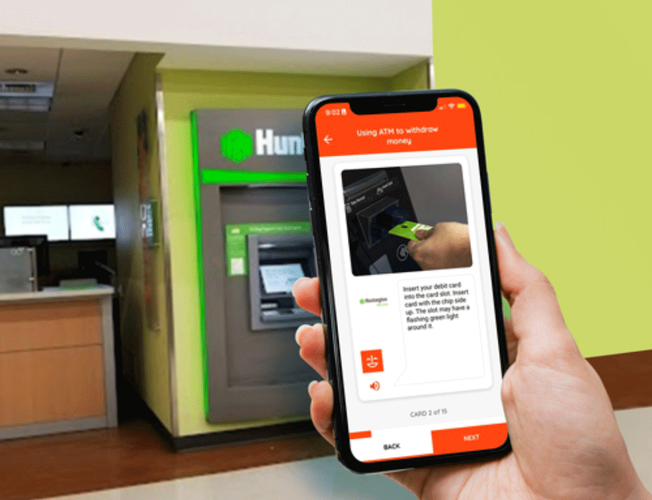 A person holding a mobile phone in front of an ATM machine.