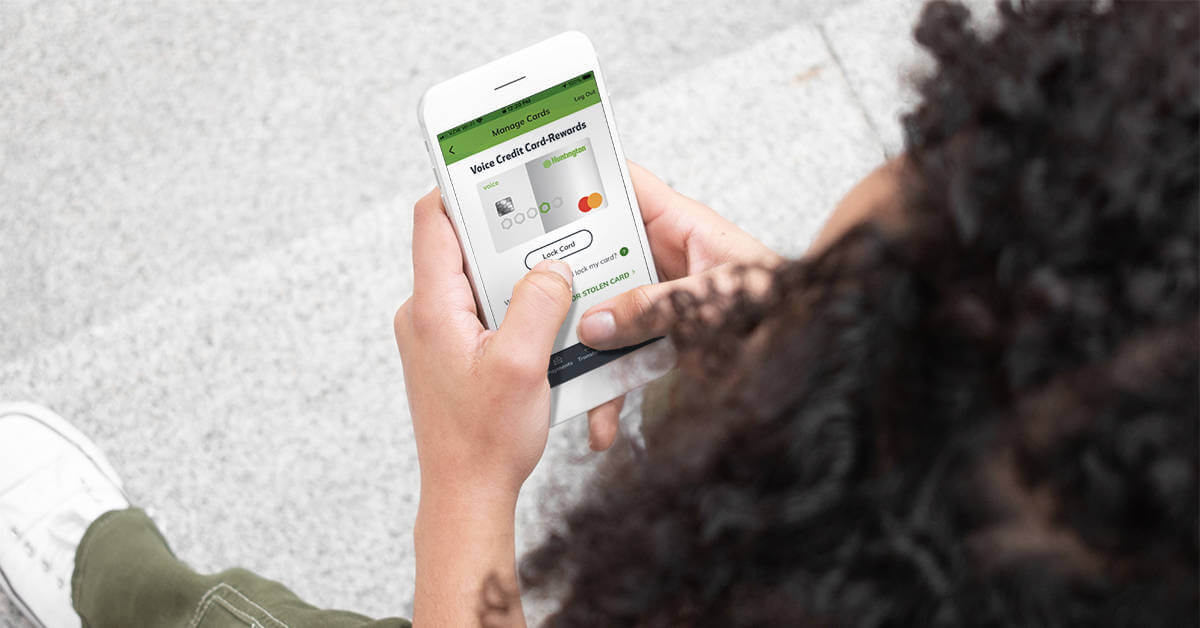 A woman sitting at a computer uses her smartphone for identity theft protection.