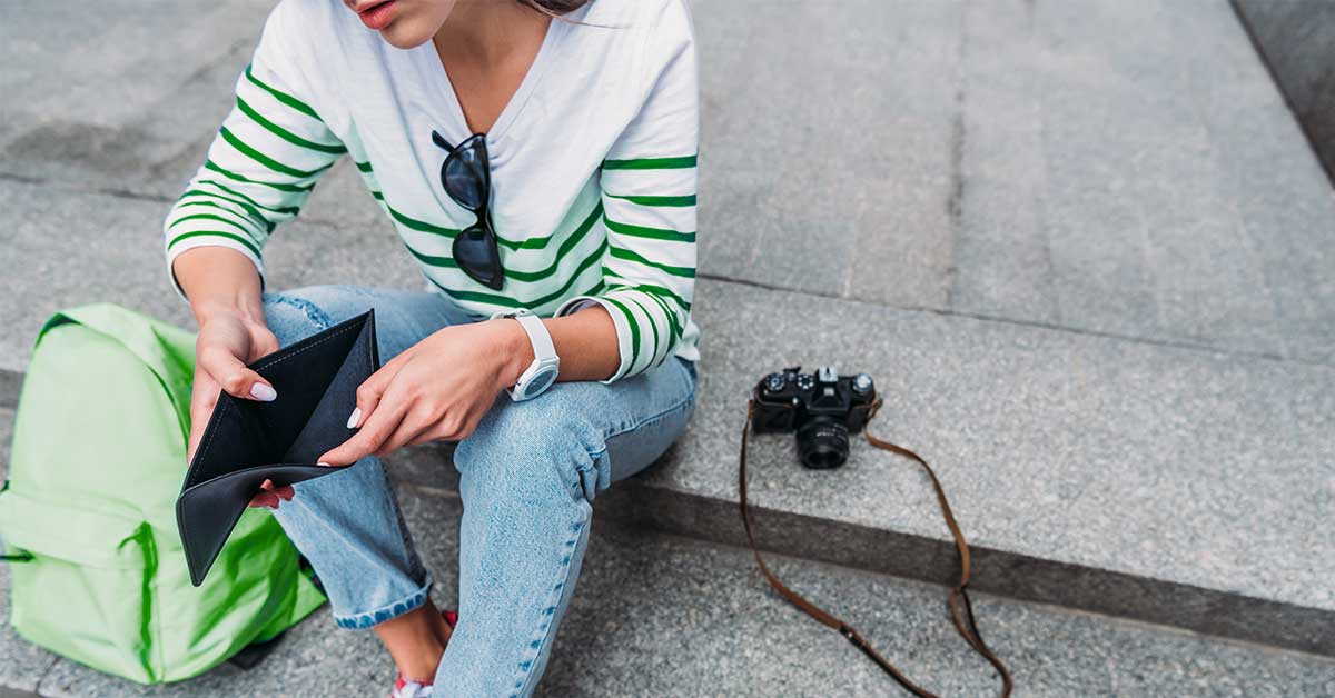 A woman is sitting on a street corner distraught, with her wallet opened, because she lost her debit card.