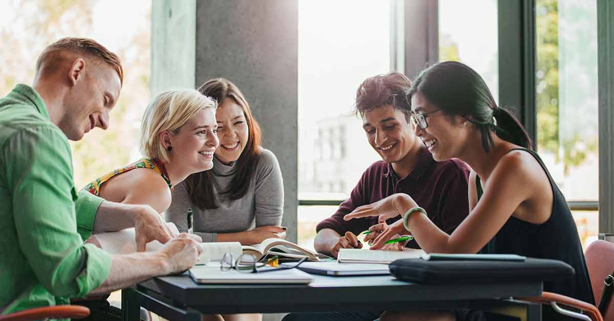 A group of young adults in their 20s sit together at a table studying for college classes and planning their financial futures. 