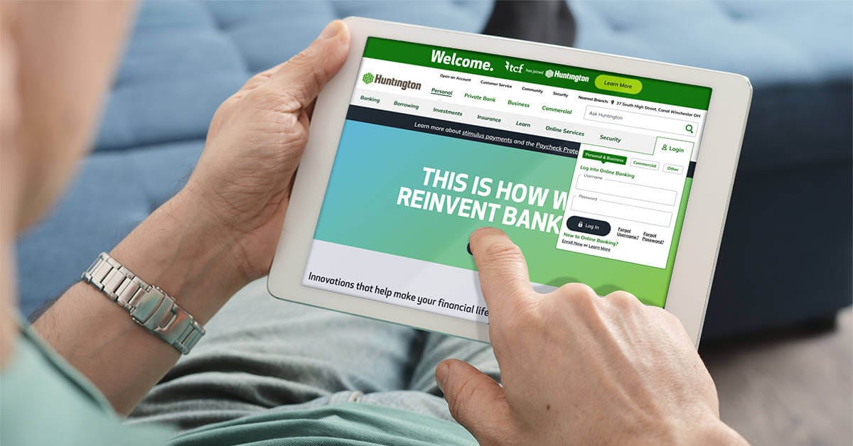 A man walking through a city looks at his smartphone to check the Huntington mobile banking app.