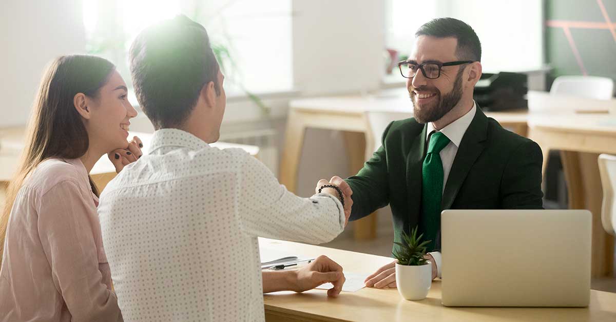 A young couple shakes hands with a bank employee as they prepare to discuss bank accounts
