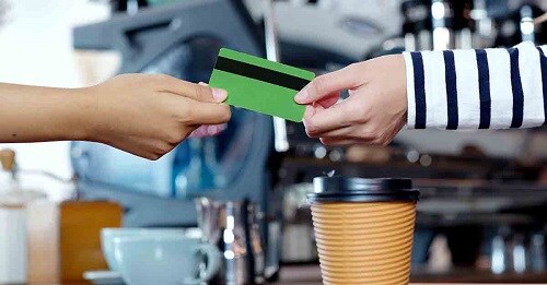 a customer hands a debit card to a barista at a coffee shop