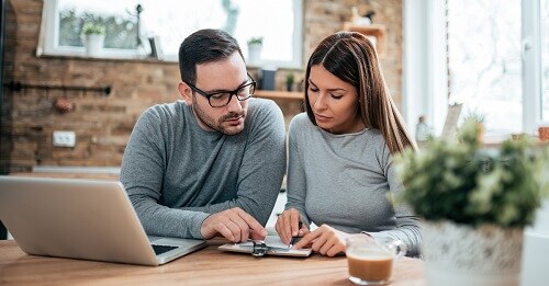 a couple uses a ledger to manually balance their checkbook