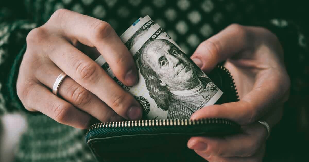 two hands pull a wad of cash out of a wallet