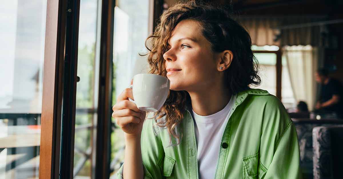 person sipping cup of coffee and looking out window