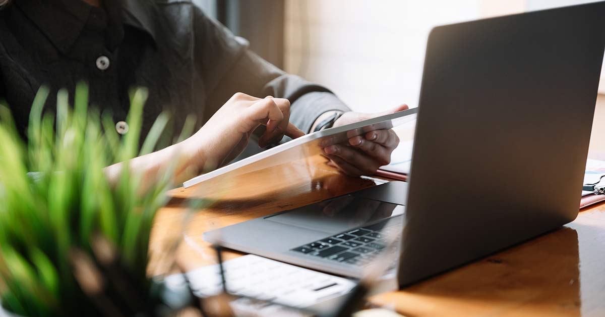 person looking at tablet in front of laptop