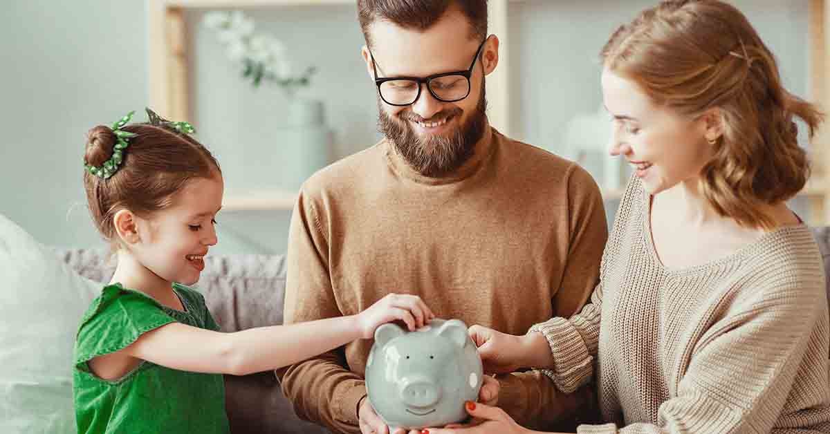 two parents let their young daughter put a coin in her piggy bank