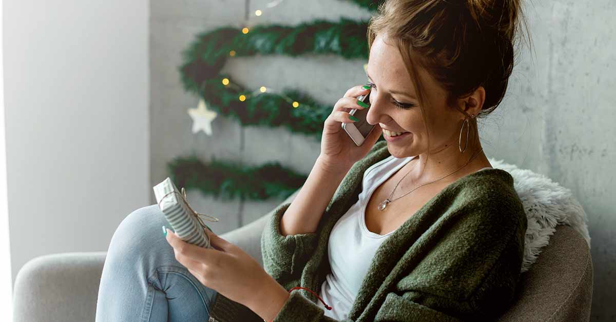 Smiling woman speaking on the phone looks at a wrapped gift she's holding