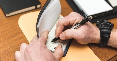 someone holds open their checkbook while writing a check