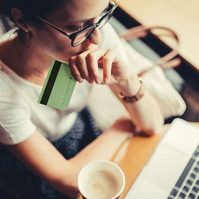 woman holds a debit card while reading a computer screen